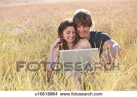 Picture - Couple using laptop in tall grass. Fotosearch