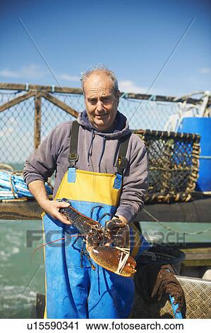 Stock Image - Fisherman holding lobster on boat. Fotosearch