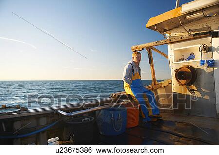 Stock Photograph - Fisherman sitting on ledge of boat. Fotosearch