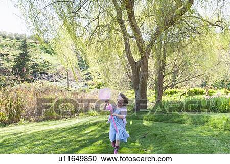 Stock Image - Girl playing with butterfly net in field. Fotosearch