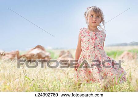 Stock Image - Girl standing in tall grass outdoors. Fotosearch