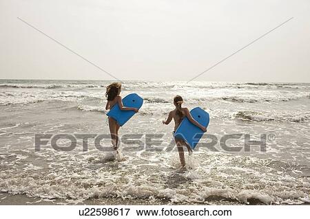Stock Photo - Girls carrying boogie boards in waves. Fotosearch