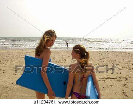 Stock Image - Girls carrying boogie boards on beach. Fotosearch