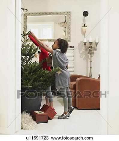 Stock Image - Girls decorating Christmas tree. Fotosearch