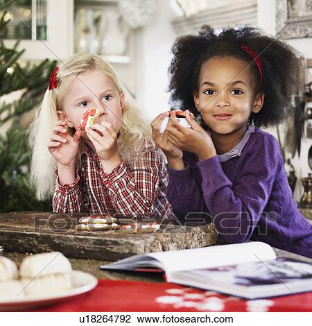 Stock Image - Girls eating Christmas cookies together. Fotosearch