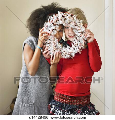 Stock Photograph - Girls peeking through Christmas wreath. Fotosearch