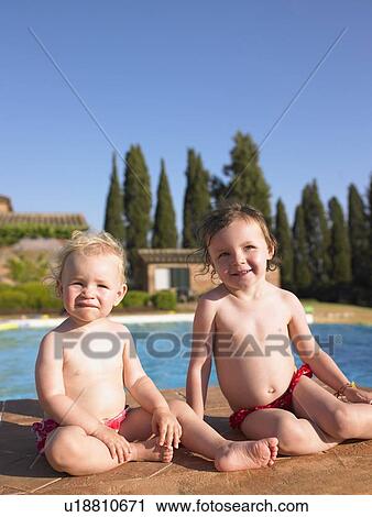 Stock Image - Girls sitting by swimming pool. Fotosearch
