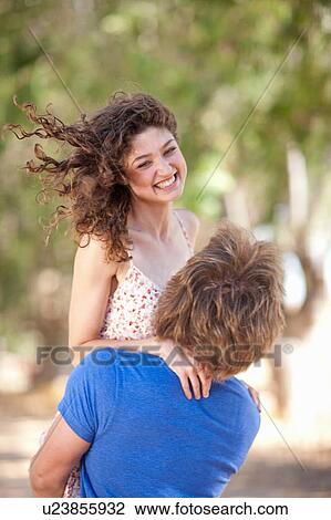 Stock Image - Man carrying girlfriend outdoors. Fotosearch