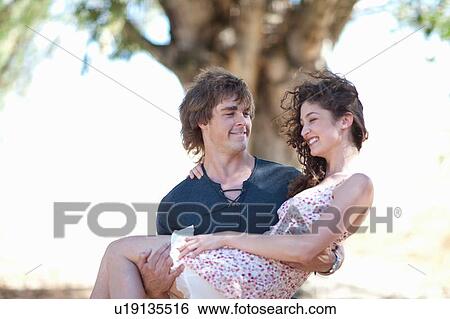Stock Photograph - Man carrying girlfriend outdoors. Fotosearch