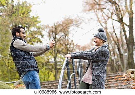 Stock Photograph - Man taking picture of girlfriend in park. Fotosearch