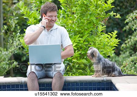 Stock Image - Man using cell phone and laptop outdoors. Fotosearch