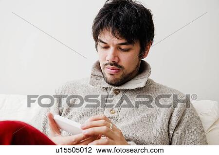 Stock Image - Man using cell phone on sofa. Fotosearch