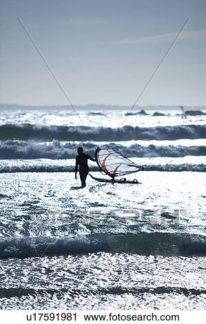 Stock Image - Man with wind sailing board in waves. Fotosearch