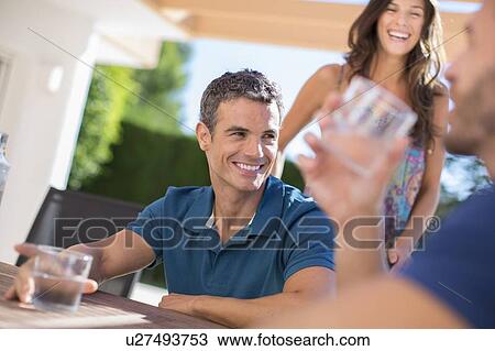 Stock Image - Men drinking water at table outdoors. Fotosearch