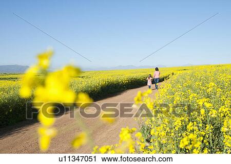 Stock Image - Mother and daughter walking on dirt road. Fotosearch