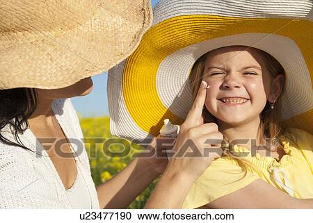 Stock Image - Mother rubbing sunscreen on daughter. Fotosearch