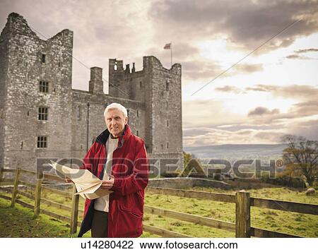 Stock Image - Older man reading map by castle. Fotosearch