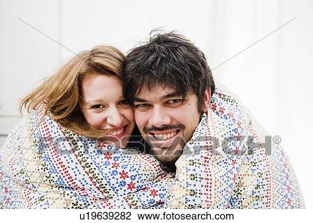 Stock Image - Smiling couple wrapped in blanket. Fotosearch