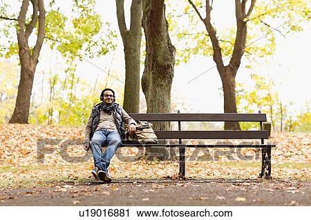 Stock Image - Smiling man sitting on park bench. Fotosearch