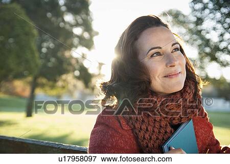 Stock Photo - Smiling woman holding book outdoors. Fotosearch