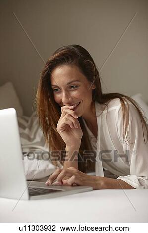 Smiling woman using laptop in bed View Large Photo Image Stock Image - Smiling woman using laptop in bed. Fotosearch