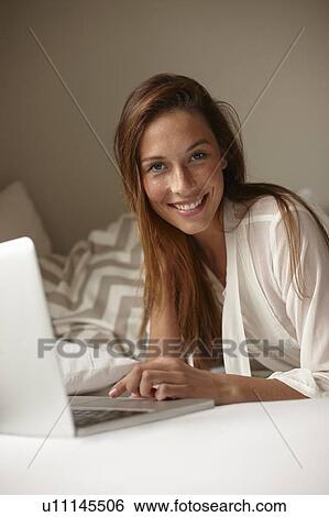 Smiling woman using laptop in bed View Large Photo Image Stock Photograph - Smiling woman using laptop in bed. Fotosearch