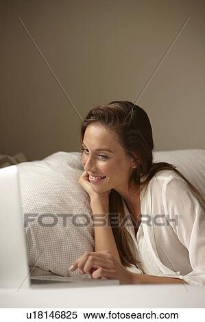 Stock Photography - Smiling woman using laptop in bed. Fotosearch