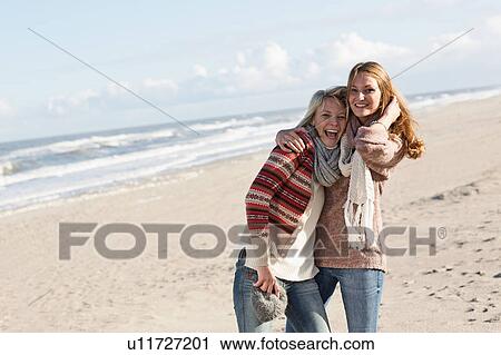 Stock Image - Smiling women hugging on beach. Fotosearch