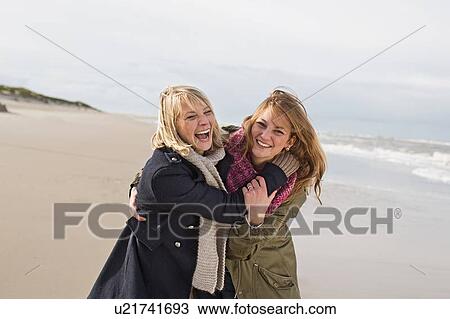 Stock Image - Smiling women hugging on beach. Fotosearch