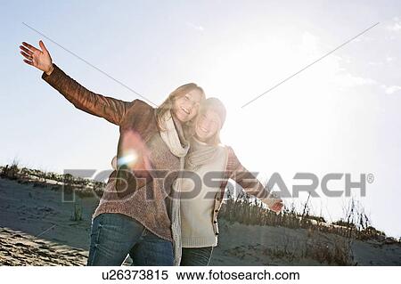 Stock Photography - Smiling women hugging on beach. Fotosearch