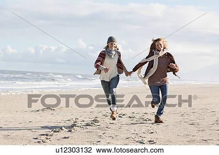 Stock Image - Smiling women running on beach. Fotosearch