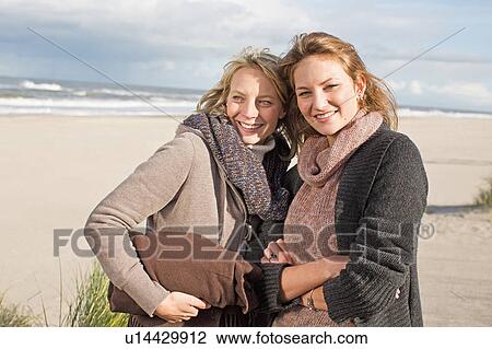 Stock Image - Smiling women standing on beach. Fotosearch
