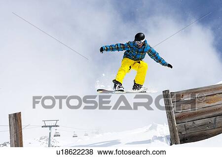 Stock Photo - Snowboarder jumping off wooden fence. Fotosearch
