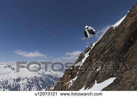 Stock Image - Snowboarder jumping on rocky slope. Fotosearch