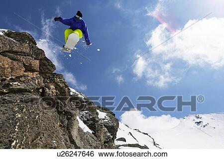 Stock Photograph - Snowboarder jumping on rocky slope. Fotosearch