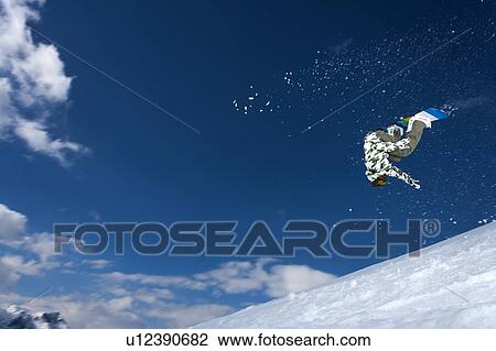 Stock Image - Snowboarder jumping on snowy slope. Fotosearch