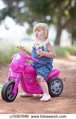 Stock Photo - Toddler girl sitting on toy motorcycle. Fotosearch
