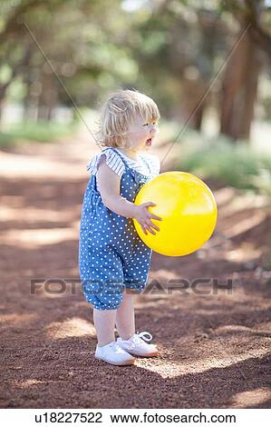 Stock Image - Toddler girl with ball on dirt road. Fotosearch