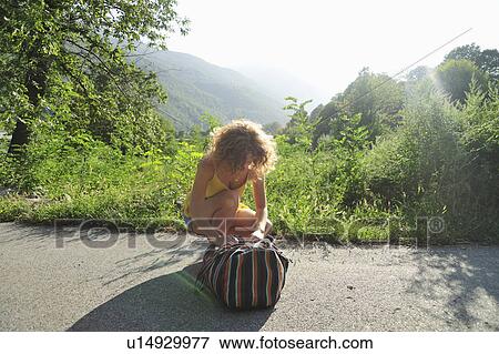 Stock Photo - Woman closing rucksack on rural road. Fotosearch