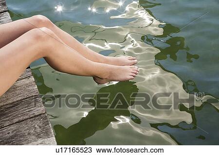 Stock Image - Woman dipping toes into still lake. Fotosearch