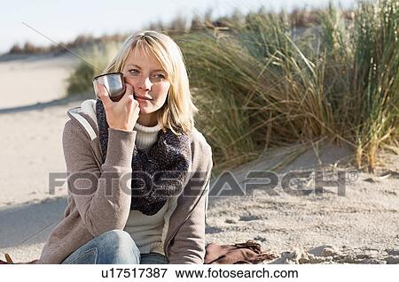 Stock Photo - Woman drinking from thermos on beach. Fotosearch