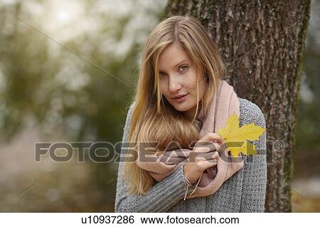 Stock Photograph - Woman holding autumn leaf outdoors. Fotosearch