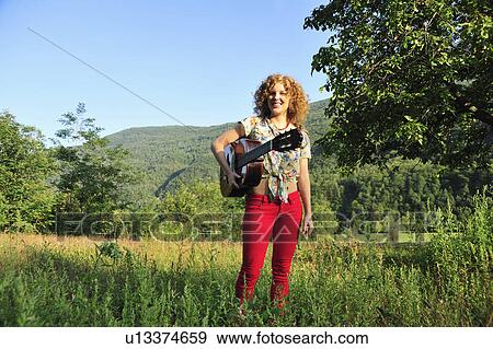 Woman holding guitar in grassy field View Large Photo Image Stock Photo - Woman holding guitar in grassy field. Fotosearch