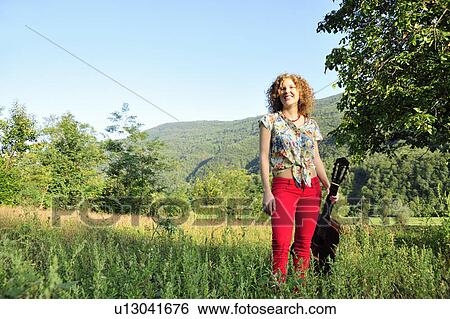 Woman holding guitar in grassy field View Large Photo Image Stock Photograph - Woman holding guitar in grassy field. Fotosearch