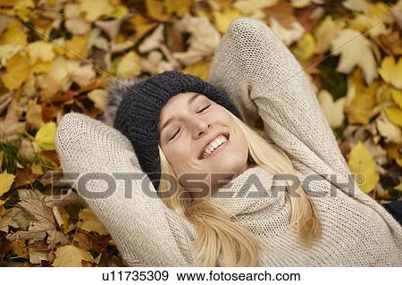 Stock Photo - Woman laying in autumn leaves outdoors. Fotosearch