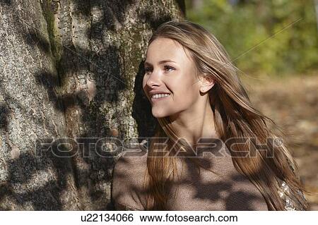 Stock Photograph - Woman leaning against tree in forest. Fotosearch