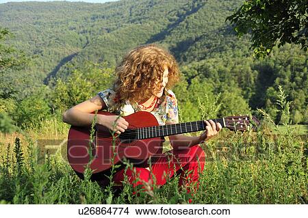 Picture - Woman playing guitar in grassy field. Fotosearch