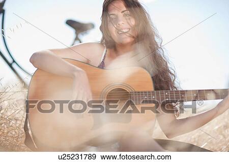 Stock Photo - Woman playing guitar in tall grass. Fotosearch
