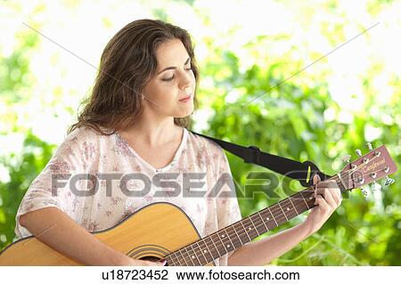 Stock Image - Woman playing guitar outdoors. Fotosearch