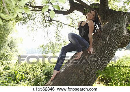 Stock Photograph - Woman sitting in tree in forest. Fotosearch